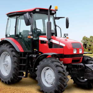 A red tractor with large tires parked on a dirt surface in daylight.